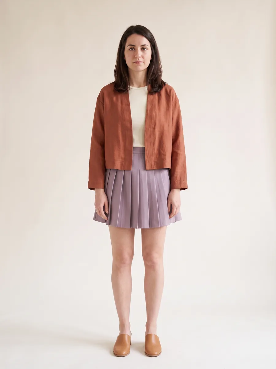 The same shopper wearing the cropped jacket with a pleated mini skirt, both ending at the waist